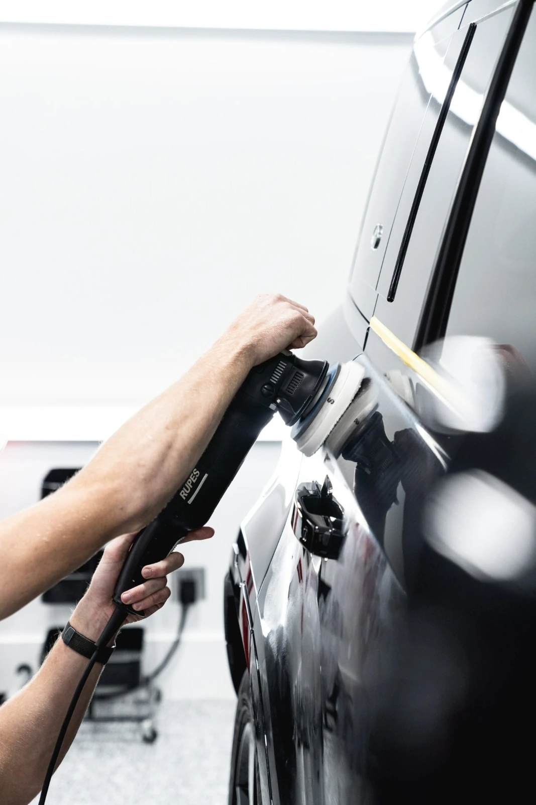 Technician using a Rupes machine polisher on a dark vehicle panel