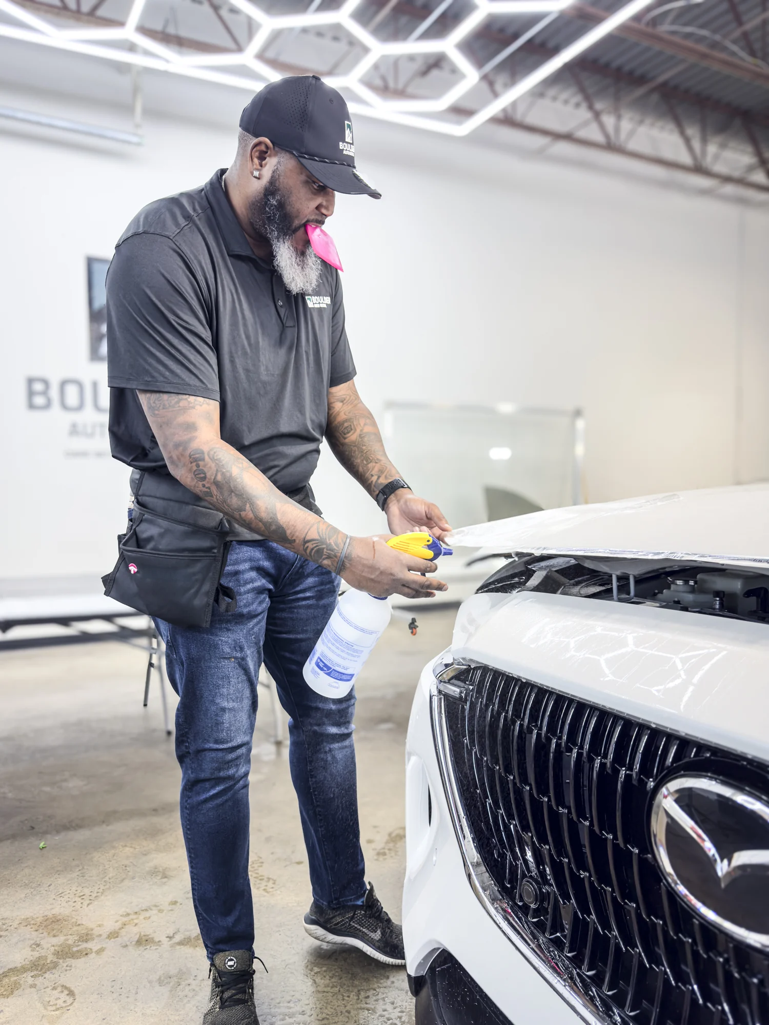 Boulder Auto Detail technician working beside a white SUV with detailing tools