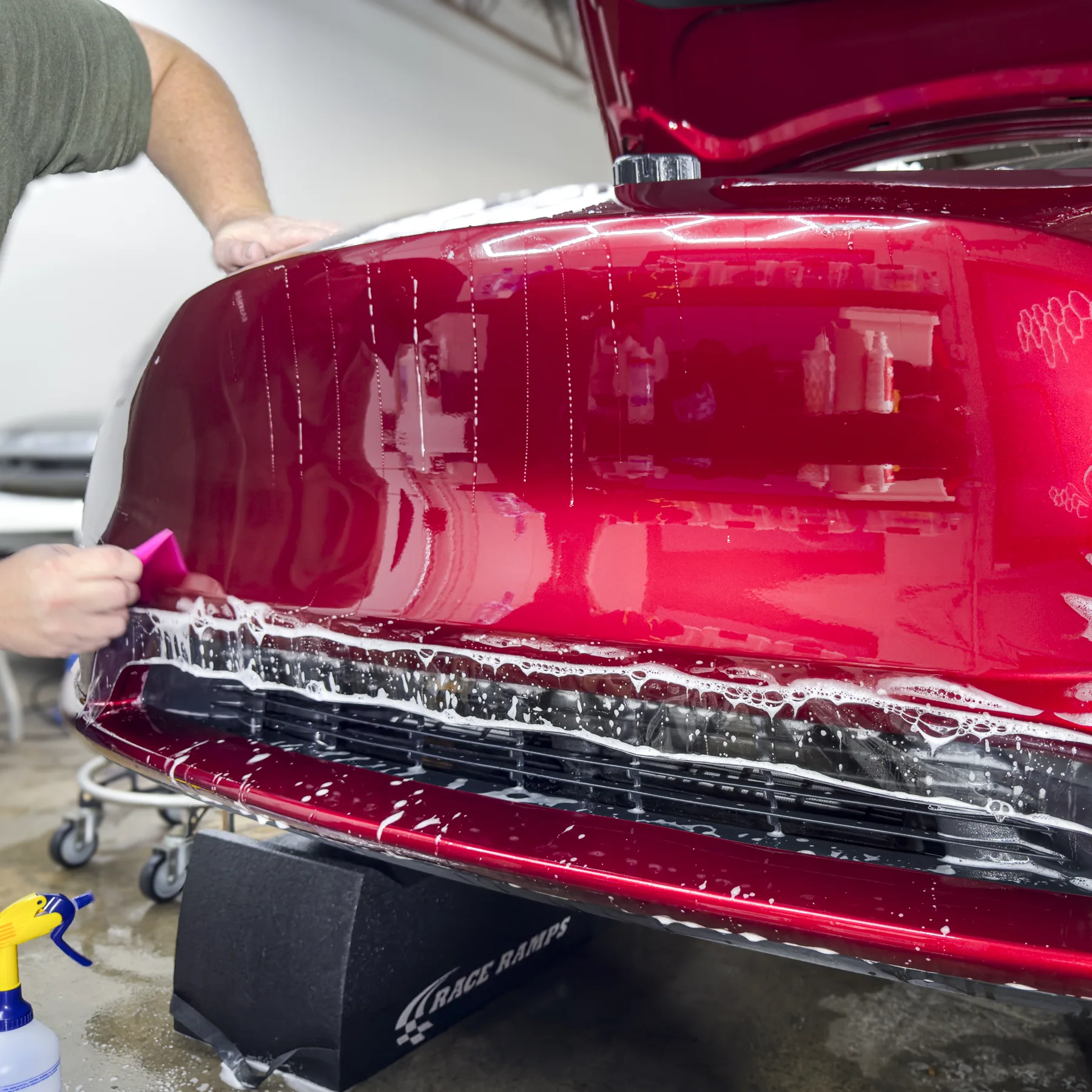 Technician installing clear paint protection film on a red Tesla bumper