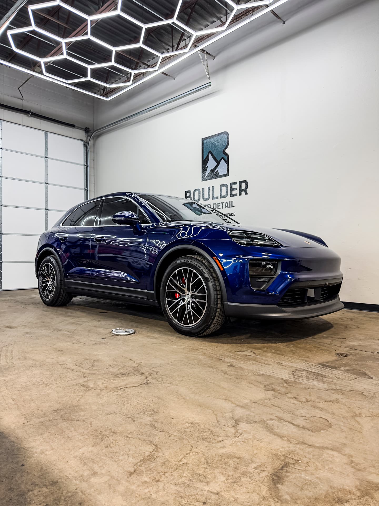 Finished blue Porsche Macan EV photographed under the hexagonal workshop lights at Boulder Auto Detail