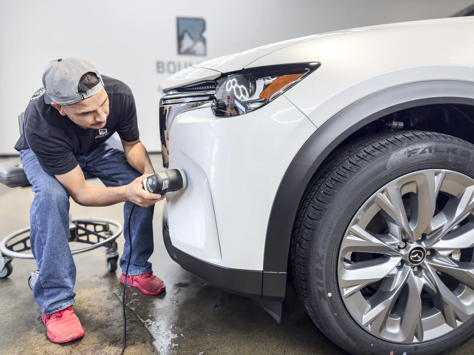 Boulder Auto Detail technician refining the front bumper of a white Mazda SUV
