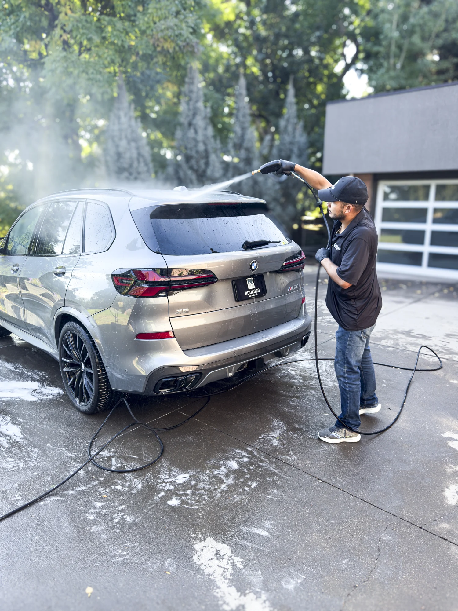 Boulder Auto Detail technician rinsing a BMW SUV in a residential driveway
